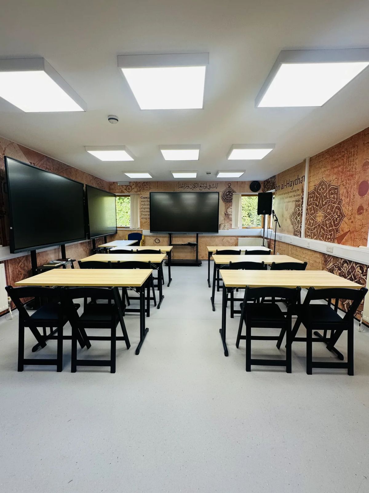 A classroom set up with desks facing three large screens